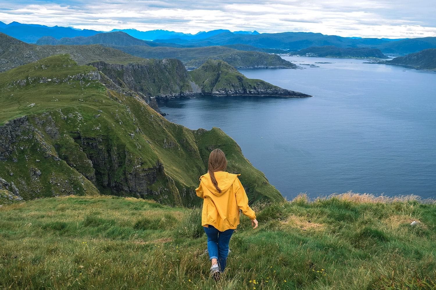 Ein Mädchen geht durch ein norwegisches Bergland mit einem atemberaubenden Blick auf das Meer und die Berge, eine unvergessliche Erfahrung während des Austauschjahres.